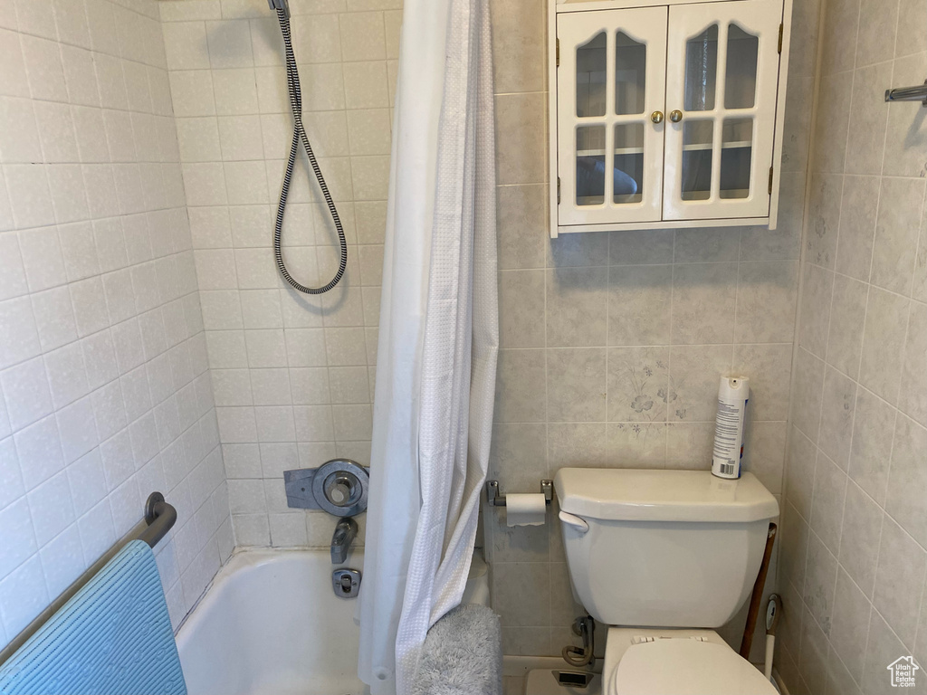 Bathroom with tile walls, shower / bath combination with curtain, and toilet