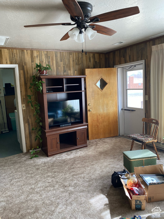 Living room with ceiling fan, a textured ceiling, carpet, and wood walls