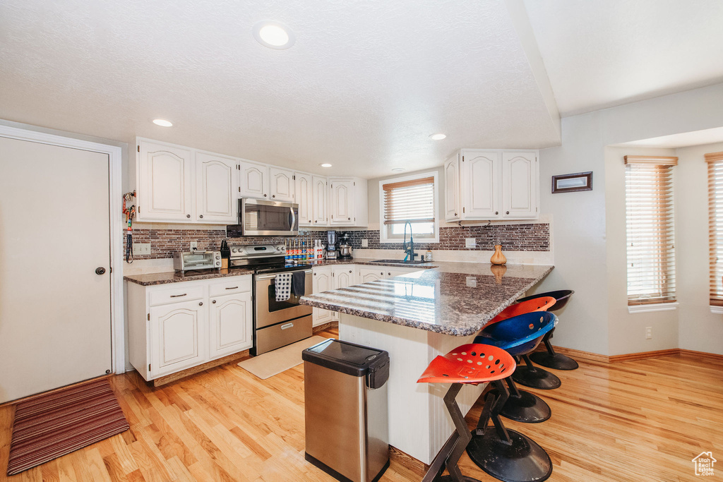 Kitchen featuring light hardwood / wood-style floors, backsplash, white cabinets, stainless steel appliances, and kitchen peninsula