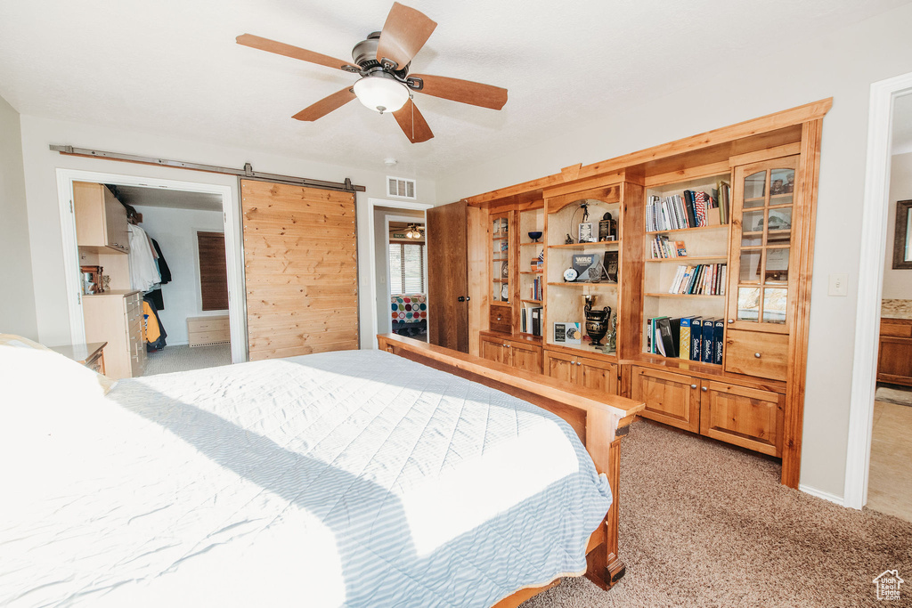 Carpeted bedroom featuring a barn door and ceiling fan
