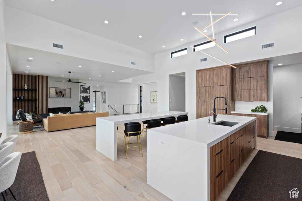 Kitchen with a breakfast bar, light hardwood / wood-style floors, a towering ceiling, sink, and a kitchen island with sink