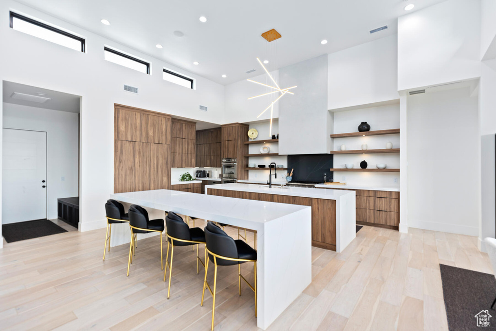 Kitchen featuring light wood-type flooring, a breakfast bar area, a kitchen island with sink, and a towering ceiling