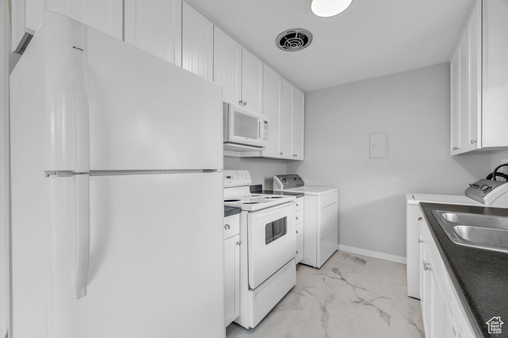Kitchen with white appliances, white cabinetry, sink, and washer and clothes dryer