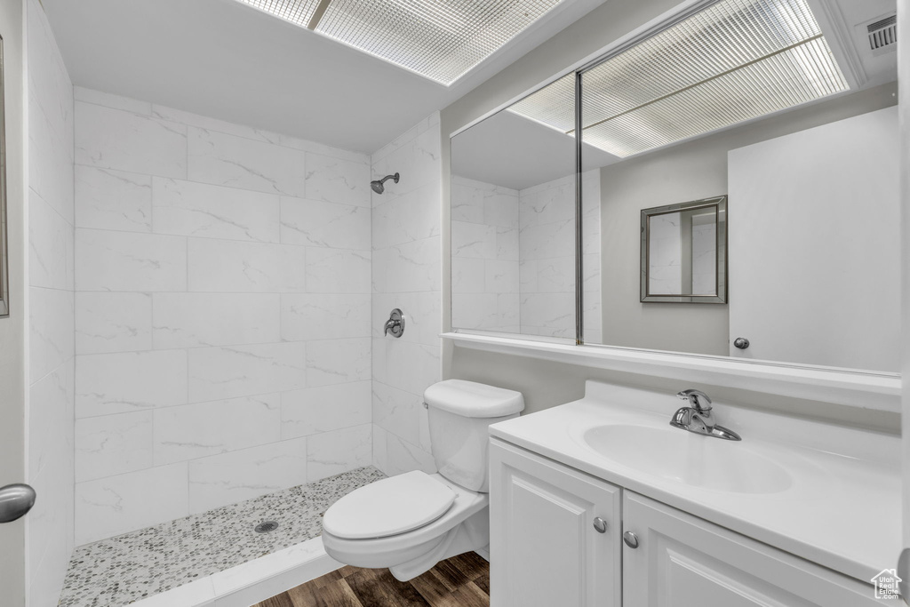 Bathroom with toilet, a tile shower, vanity with extensive cabinet space, and wood-type flooring