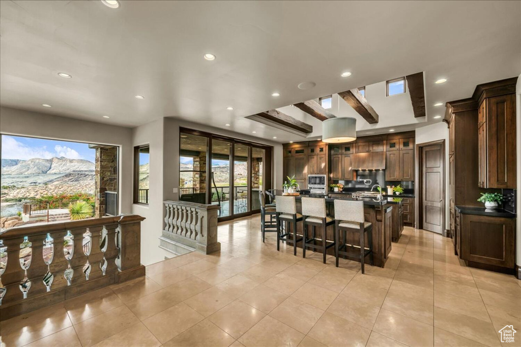 Kitchen with a kitchen island with sink, a kitchen breakfast bar, a mountain view, beamed ceiling, and light tile floors