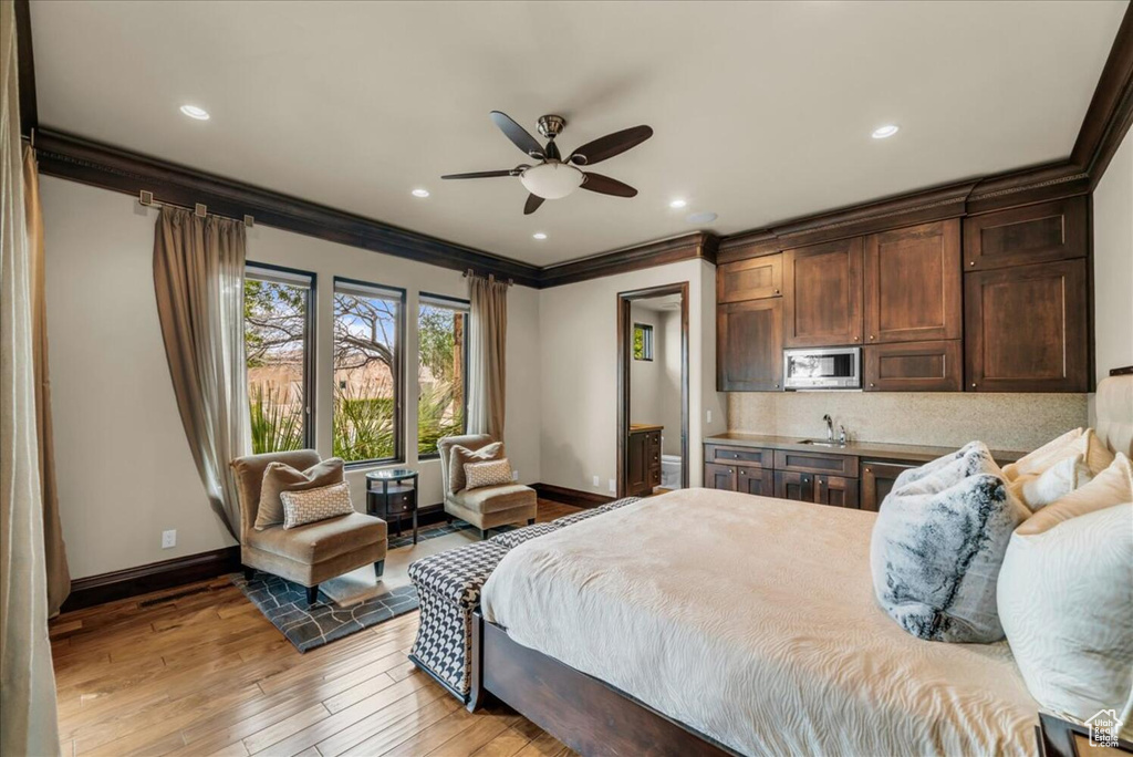Bedroom with light wood-type flooring, ornamental molding, ensuite bath, sink, and ceiling fan
