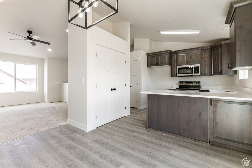 Kitchen featuring light hardwood / wood-style floors, vaulted ceiling, ceiling fan with notable chandelier, dark brown cabinets, and appliances with stainless steel finishes