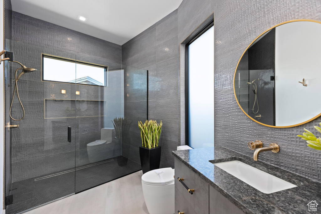 Bathroom with tile walls, a shower with door, large vanity, toilet, and tasteful backsplash