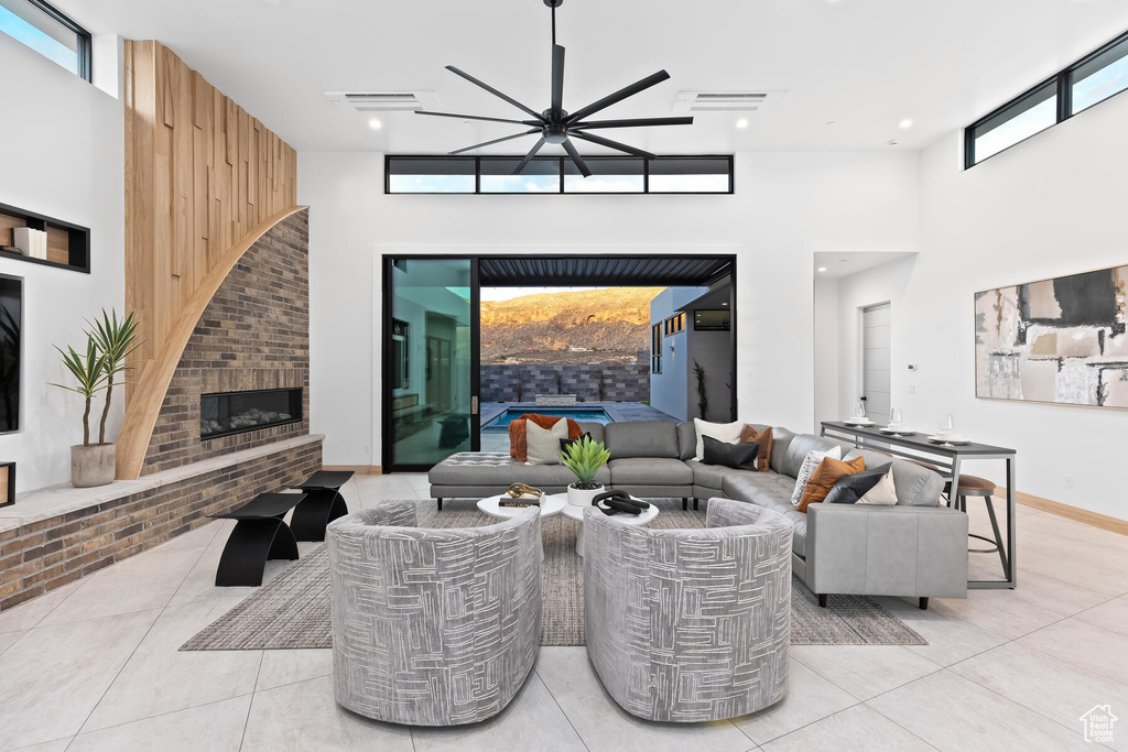 Living room featuring ceiling fan, plenty of natural light, a fireplace, and a towering ceiling