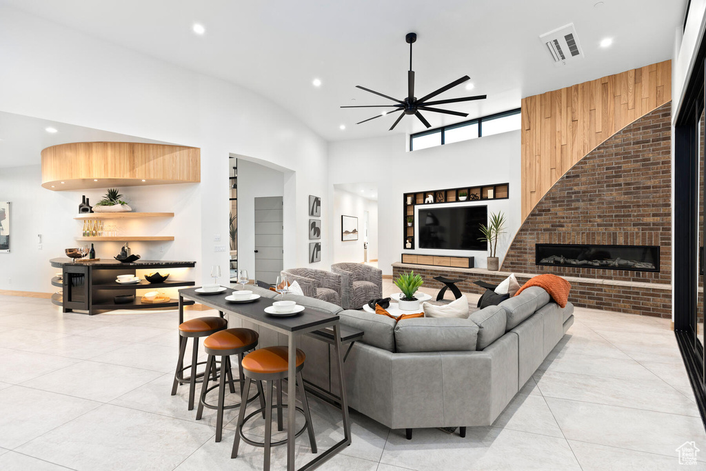 Tiled living room featuring ceiling fan, a high ceiling, and a fireplace