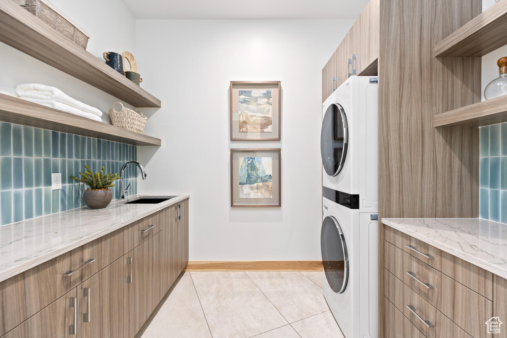 Washroom featuring sink, stacked washer / dryer, light tile floors, and cabinets