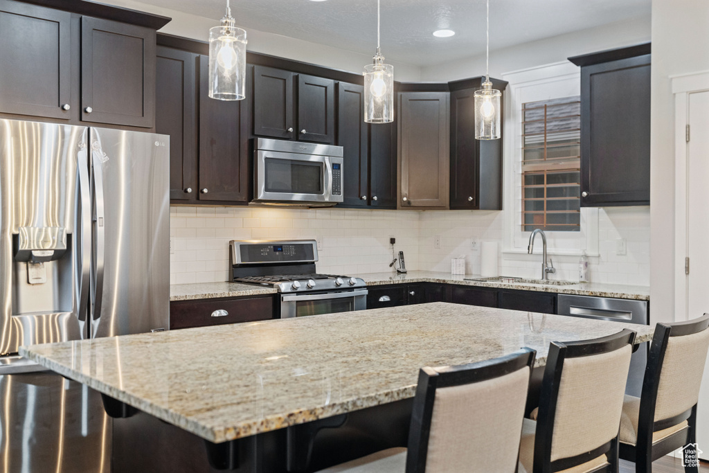 Kitchen featuring tasteful backsplash, appliances with stainless steel finishes, a breakfast bar, and pendant lighting