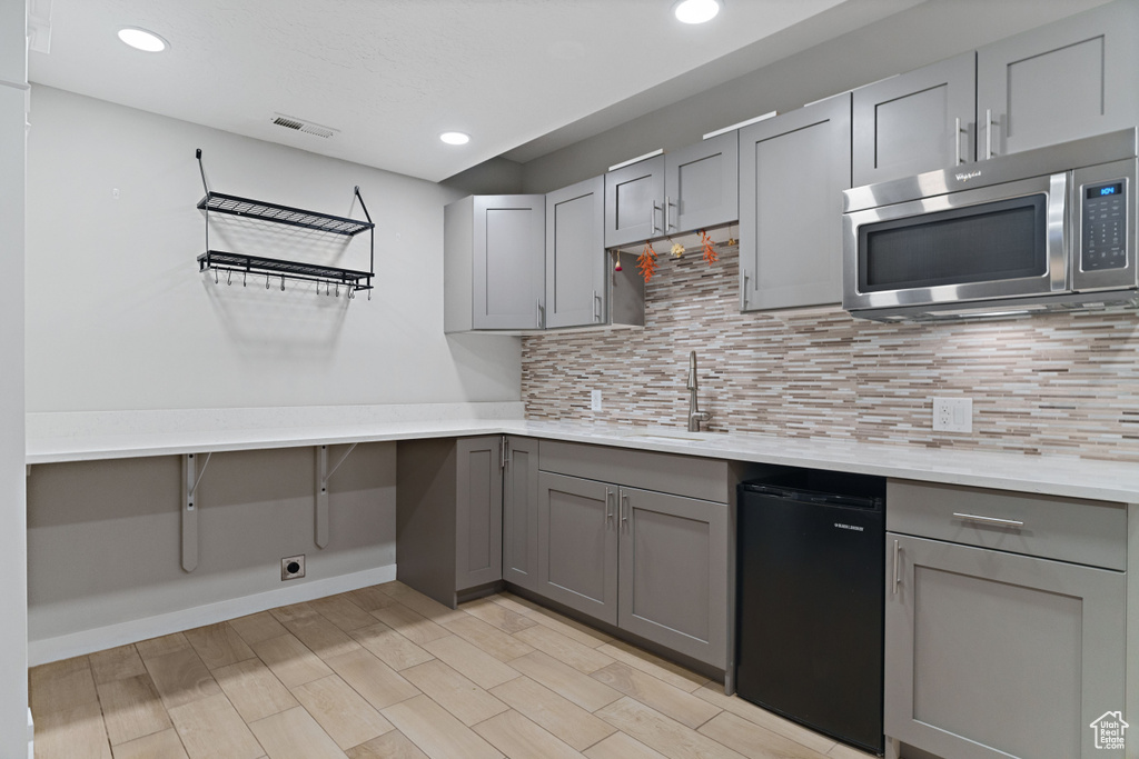 Kitchen featuring light hardwood / wood-style flooring, gray cabinetry, dishwasher, and backsplash
