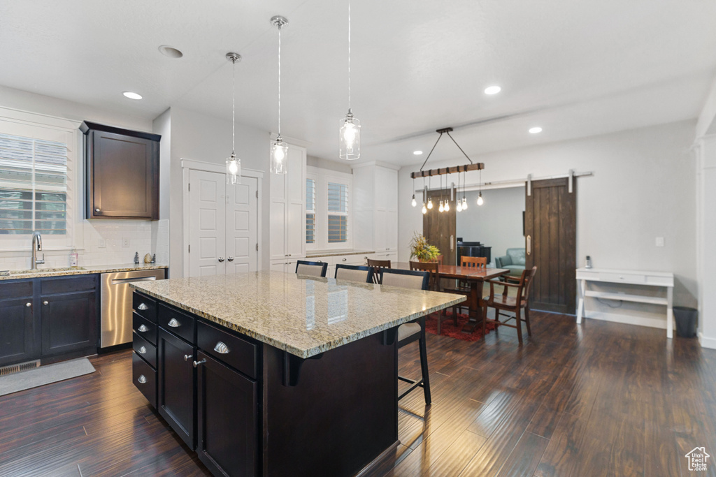 Kitchen featuring a breakfast bar area, a center island, a barn door, decorative light fixtures, and stainless steel dishwasher