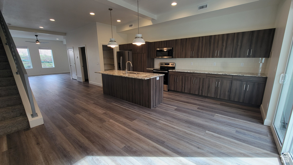 Kitchen with a kitchen island with sink, hanging light fixtures, tasteful backsplash, hardwood / wood-style floors, and appliances with stainless steel finishes