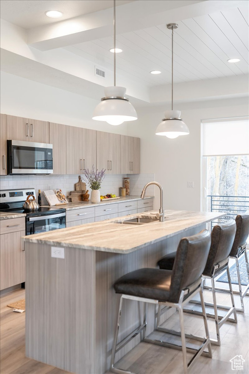 Kitchen with a kitchen island with sink, tasteful backsplash, a breakfast bar, stainless steel appliances, and pendant lighting