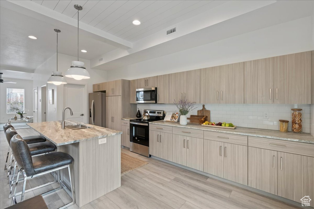 Kitchen featuring stainless steel appliances, light stone countertops, a breakfast bar, hanging light fixtures, and sink