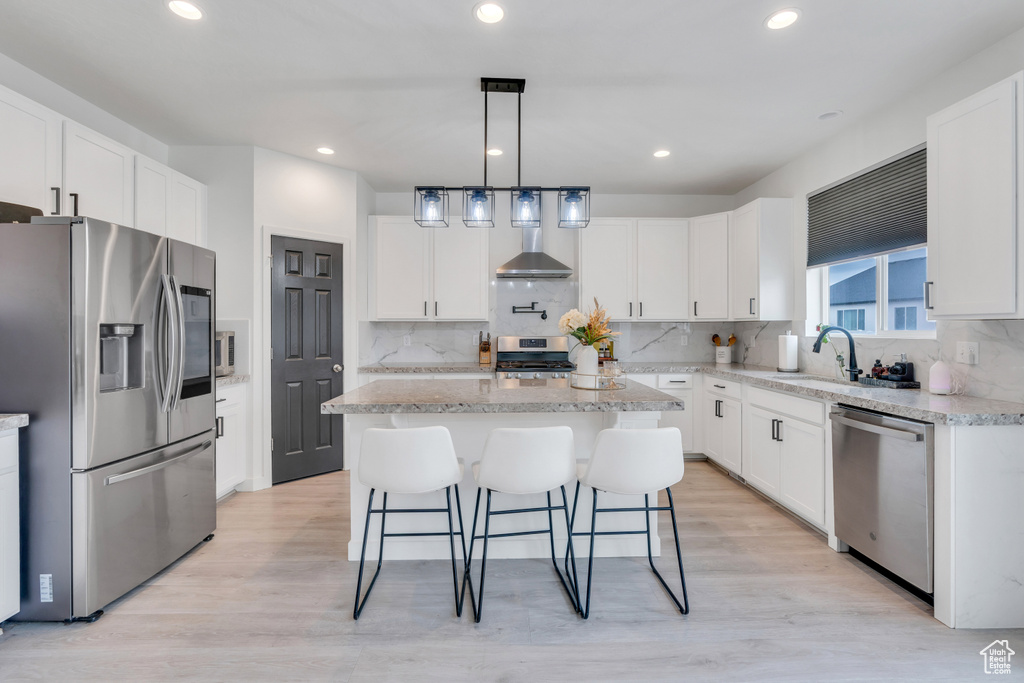 Kitchen featuring a kitchen island, tasteful backsplash, appliances with stainless steel finishes, light hardwood / wood-style flooring, and decorative light fixtures