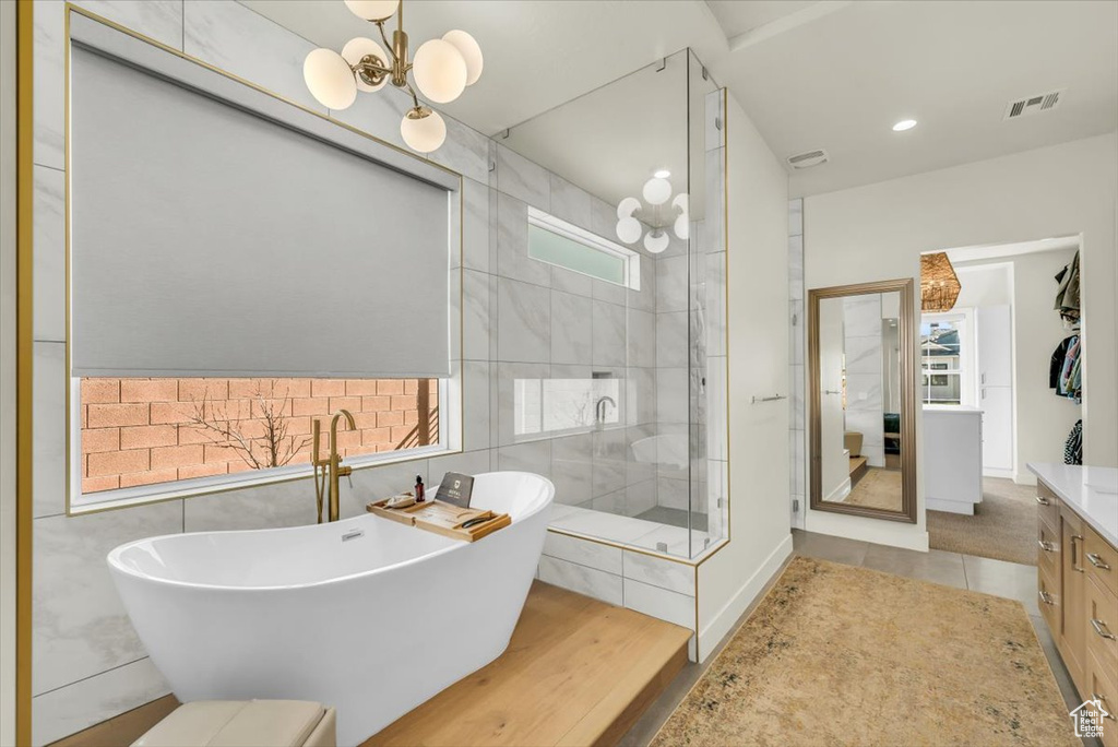 Bathroom with an inviting chandelier, separate shower and tub, vanity, tile floors, and tile walls