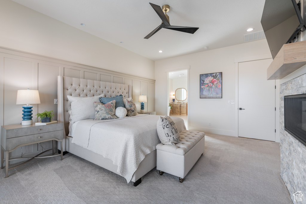 Carpeted bedroom with ensuite bath, ceiling fan, and a tile fireplace