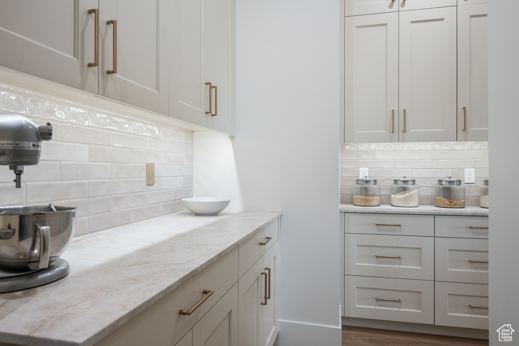 Kitchen with white cabinets, light stone counters, dark hardwood / wood-style floors, and tasteful backsplash