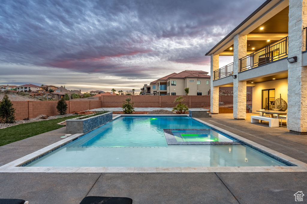 Pool at dusk featuring a patio and an in ground hot tub