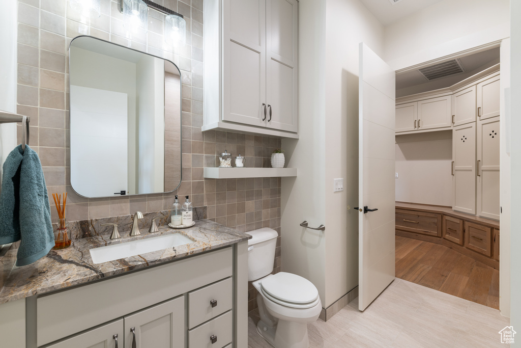 Bathroom with hardwood / wood-style floors, tasteful backsplash, toilet, tile walls, and vanity with extensive cabinet space