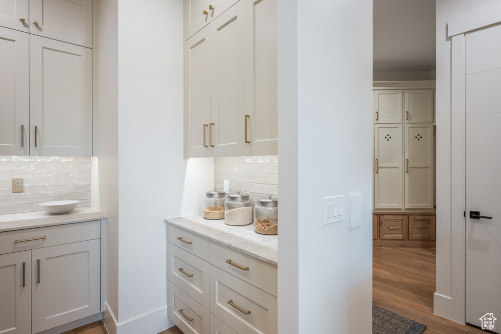 Interior space featuring white cabinetry, light stone countertops, hardwood / wood-style flooring, and backsplash