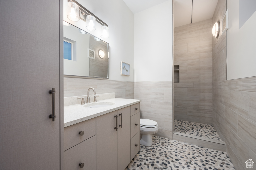 Bathroom featuring tiled shower, toilet, tile walls, large vanity, and tile floors