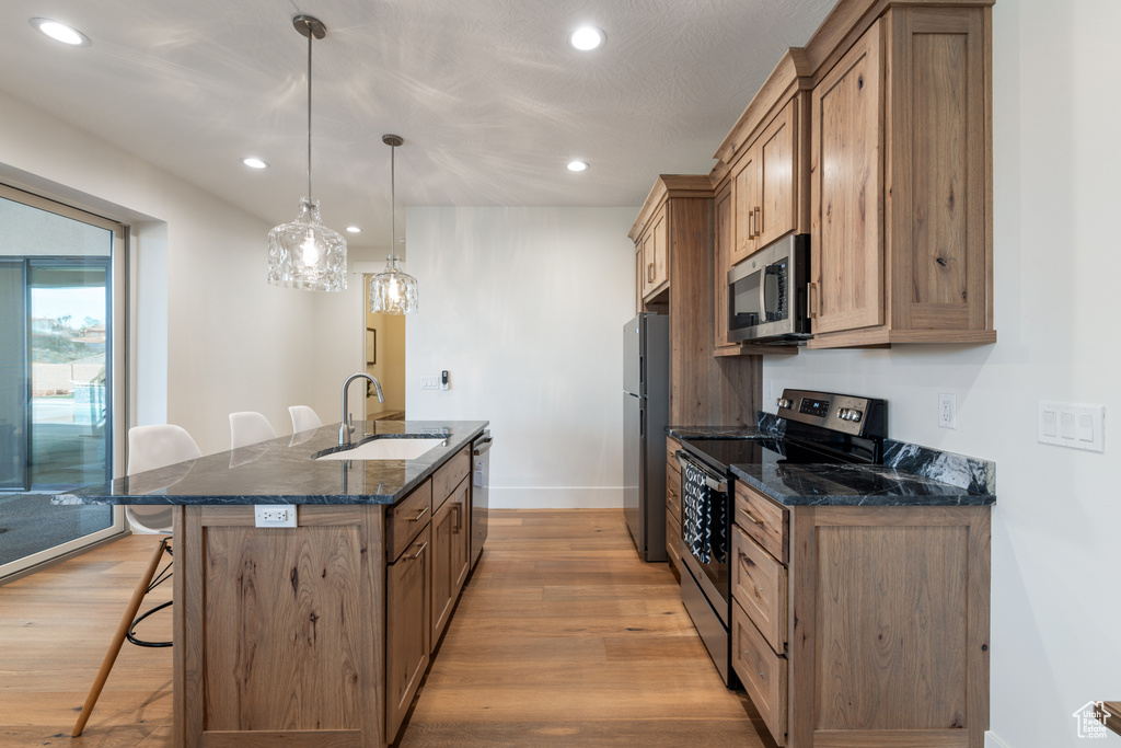 Kitchen featuring light wood-type flooring, a breakfast bar, hanging light fixtures, appliances with stainless steel finishes, and sink