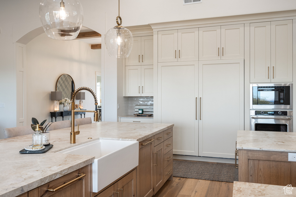 Kitchen with light hardwood / wood-style flooring, backsplash, light stone countertops, decorative light fixtures, and beam ceiling