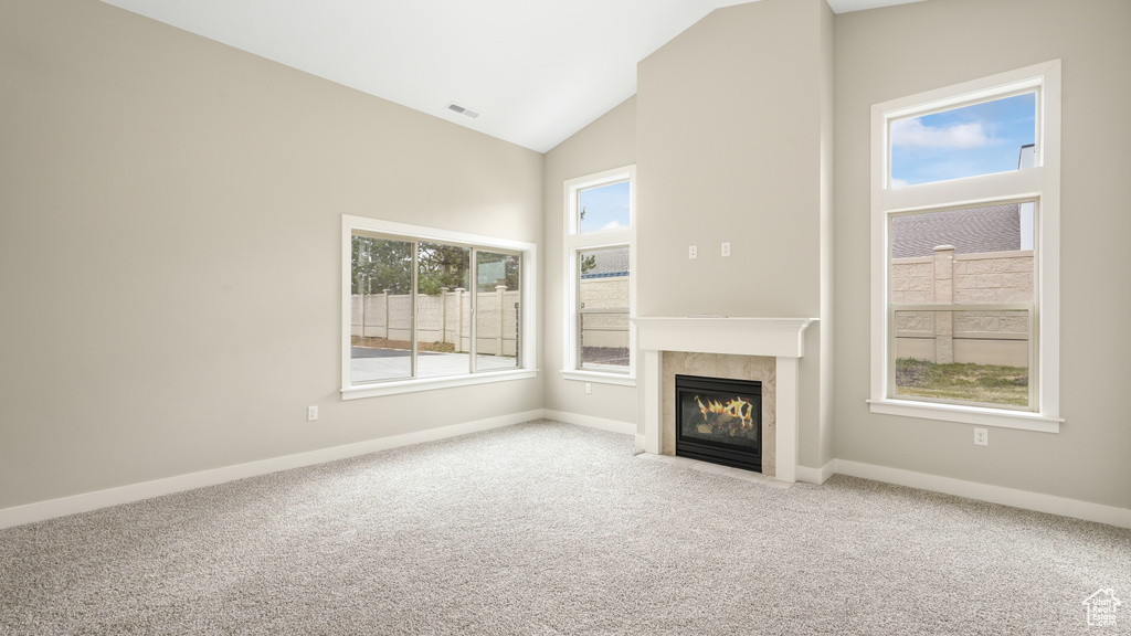 Unfurnished living room featuring high vaulted ceiling, light colored carpet, and a healthy amount of sunlight