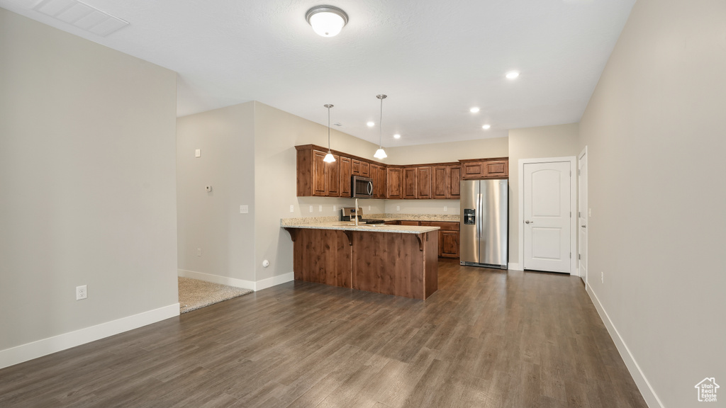 Kitchen with pendant lighting, dark hardwood / wood-style flooring, a breakfast bar area, kitchen peninsula, and appliances with stainless steel finishes