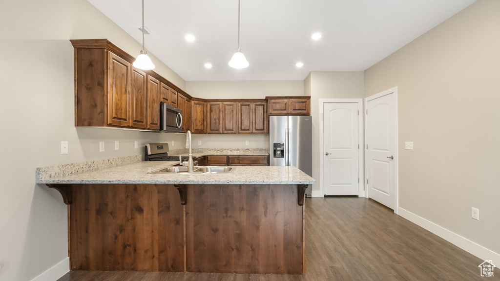 Kitchen with a breakfast bar area, hanging light fixtures, dark hardwood / wood-style floors, sink, and stainless steel appliances