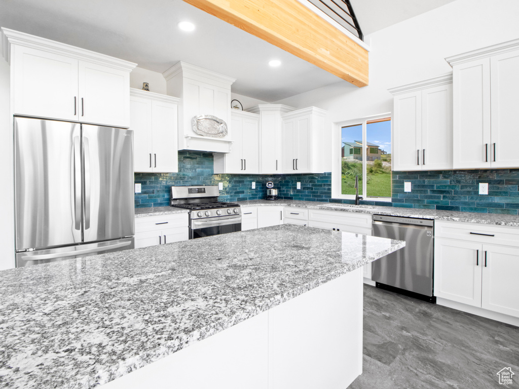 Kitchen featuring white cabinets, appliances with stainless steel finishes, light stone countertops, and backsplash