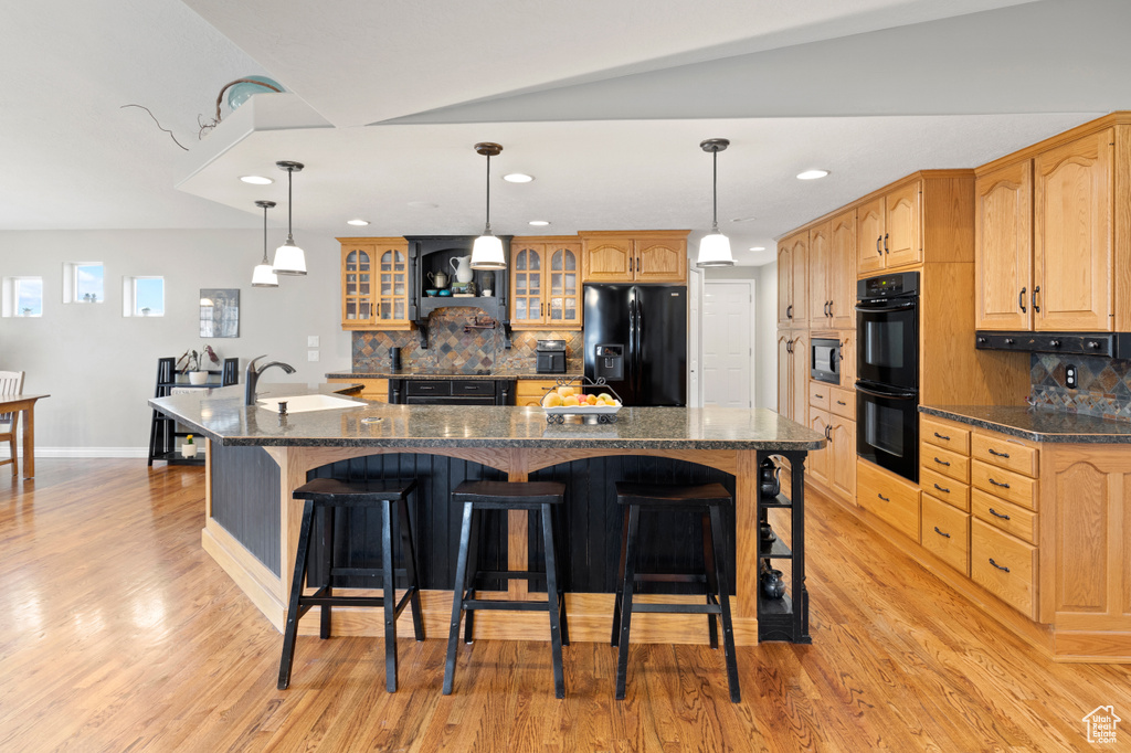 Kitchen with a center island with sink, black appliances, light wood-type flooring, a breakfast bar area, and tasteful backsplash