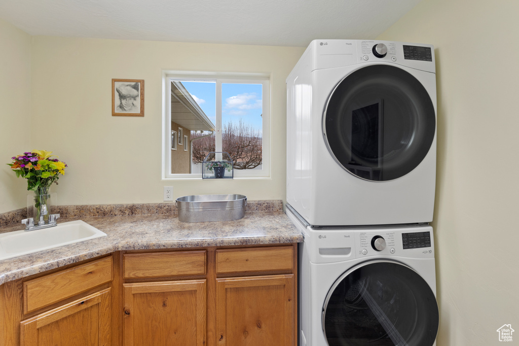 Laundry area featuring cabinets, sink, and stacked washer and clothes dryer