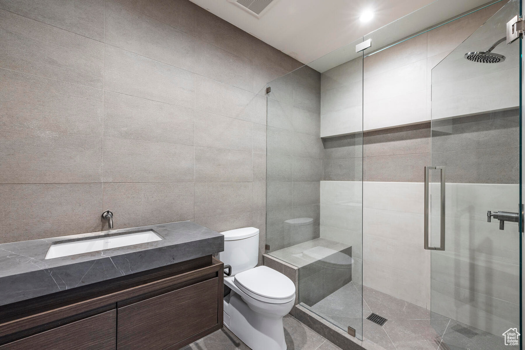 Bathroom with tile walls, tile flooring, a shower with door, vanity, and toilet