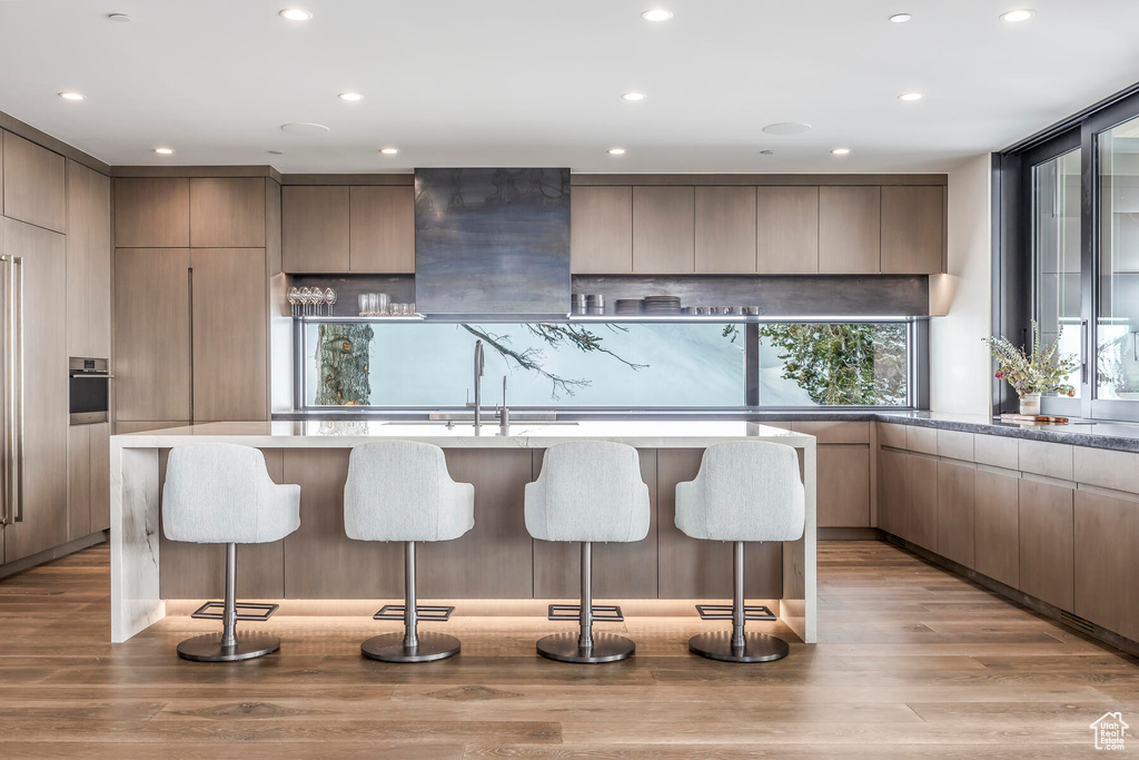 Kitchen featuring an island with sink, backsplash, a breakfast bar area, and light hardwood / wood-style floors