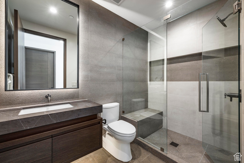 Bathroom with vanity, tile walls, toilet, tile floors, and a shower with shower door