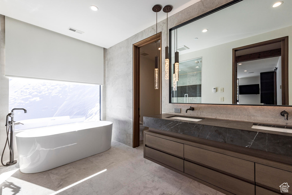 Bathroom featuring dual bowl vanity, tile floors, and a tub