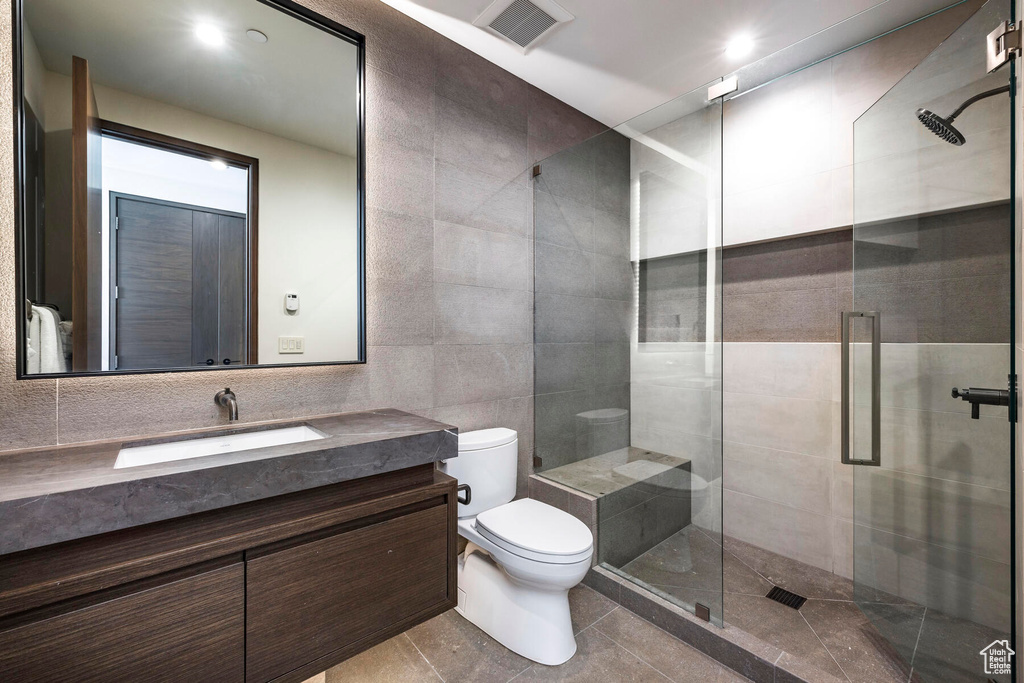 Bathroom with an enclosed shower, vanity, tile walls, toilet, and tile floors