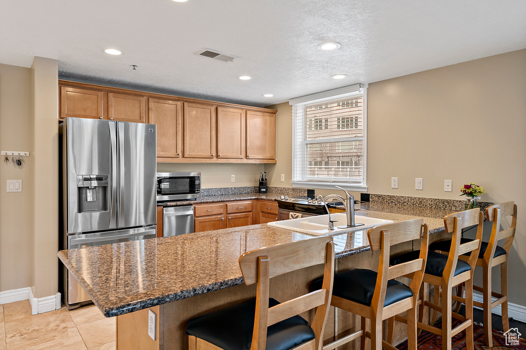 Kitchen featuring a kitchen breakfast bar, sink, light tile floors, stainless steel appliances, and kitchen peninsula