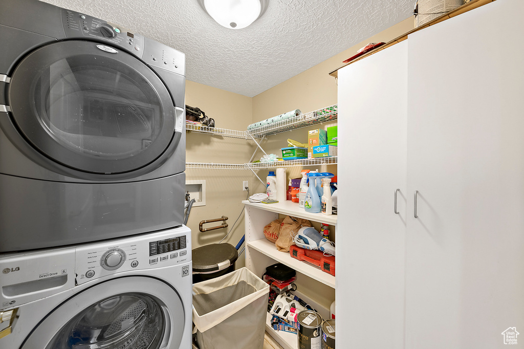 Laundry area featuring hookup for a washing machine, a textured ceiling, and stacked washer and dryer