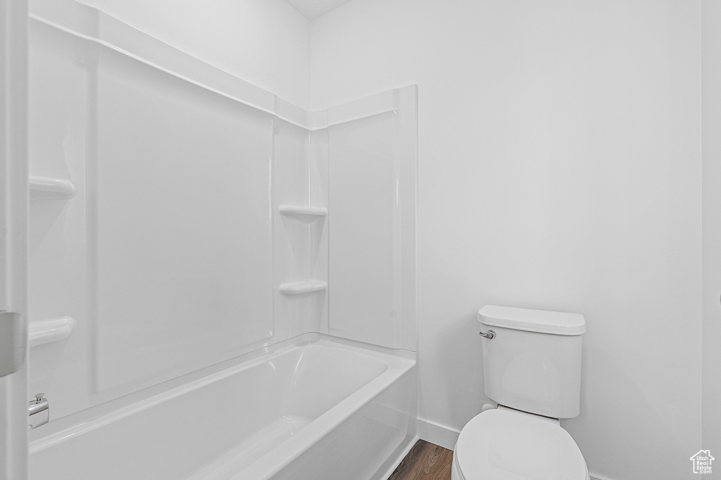 Bathroom with hardwood / wood-style floors, shower / bathing tub combination, and toilet