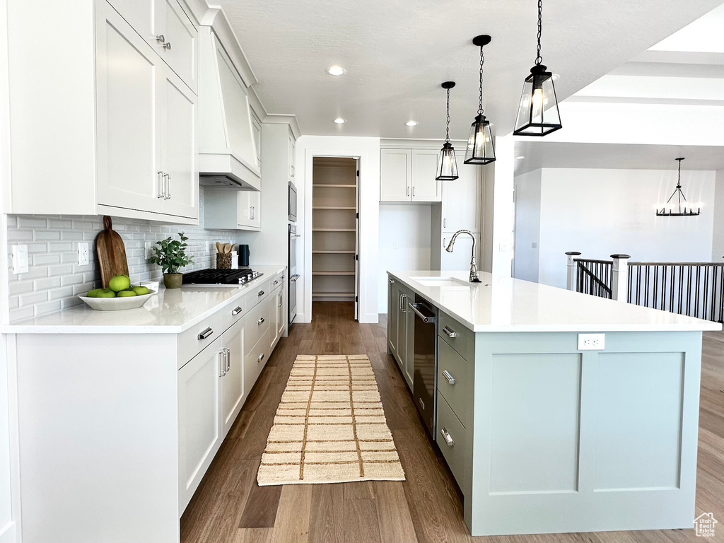Kitchen with custom range hood, pendant lighting, dark wood-type flooring, backsplash, and a kitchen island with sink