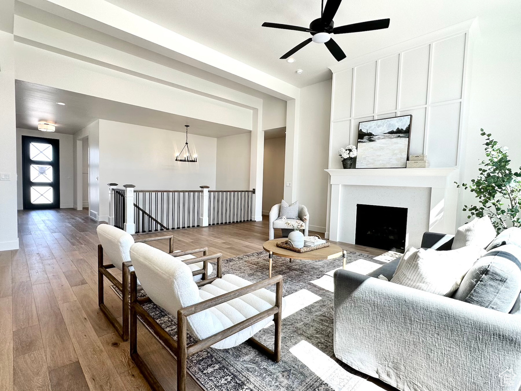 Living room with ceiling fan with notable chandelier and hardwood / wood-style flooring