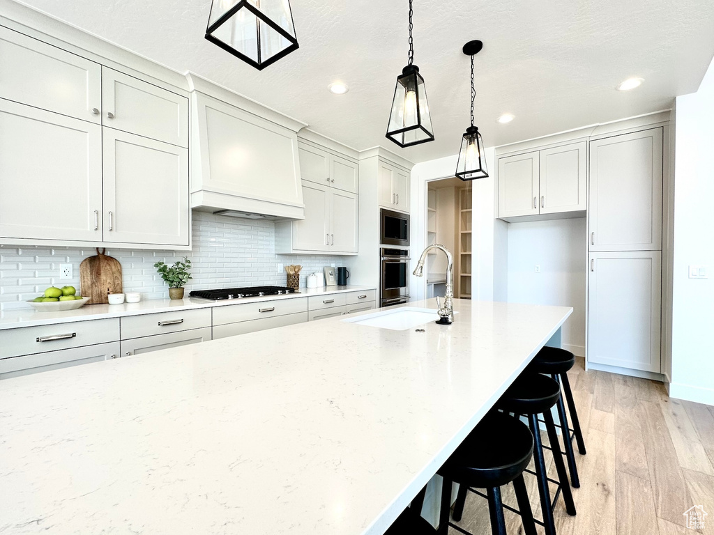 Kitchen with a breakfast bar area, backsplash, decorative light fixtures, custom exhaust hood, and light hardwood / wood-style flooring