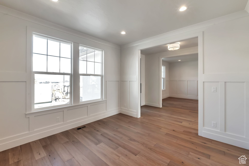 Empty room featuring light wood-type flooring, a wealth of natural light, and ornamental molding