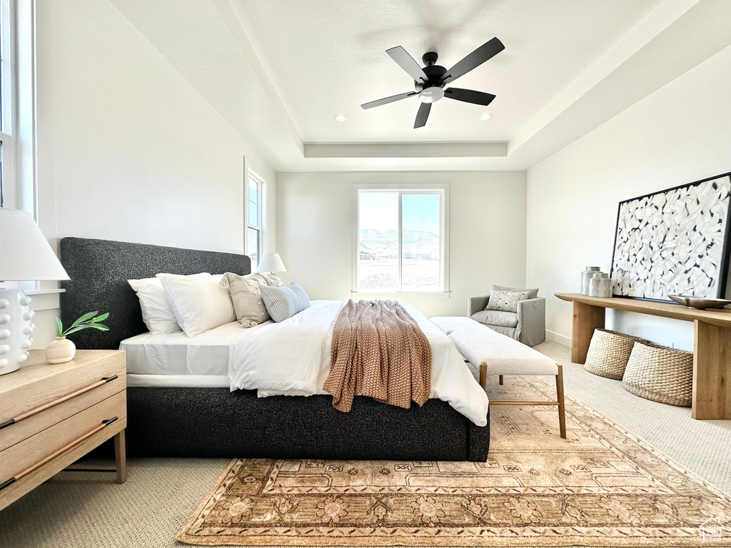 Carpeted bedroom featuring ceiling fan and a raised ceiling